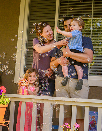 Woman and man with two young children playing soap bubbles on a porch