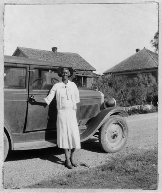Historic photo of woman standing in front of a car