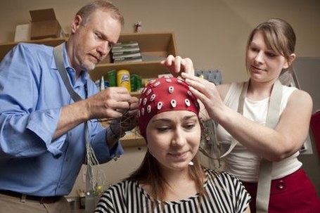 Photo of researchers attaching electrodes to a cap on someone's head. 