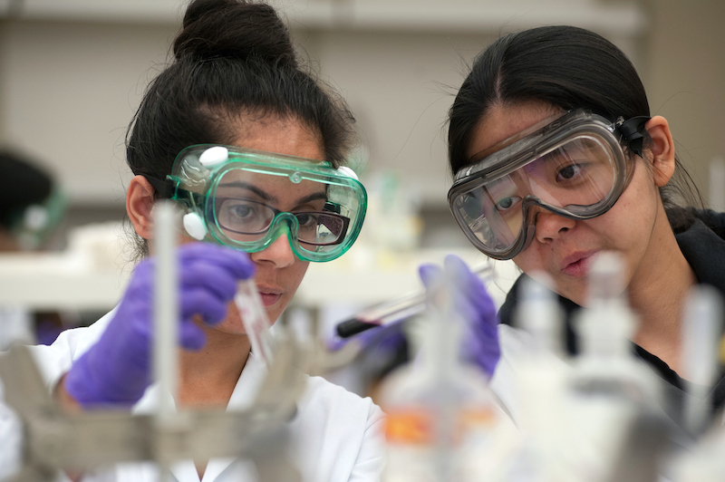 Two female students wearing protective glasses work in a chemistry laboratory.