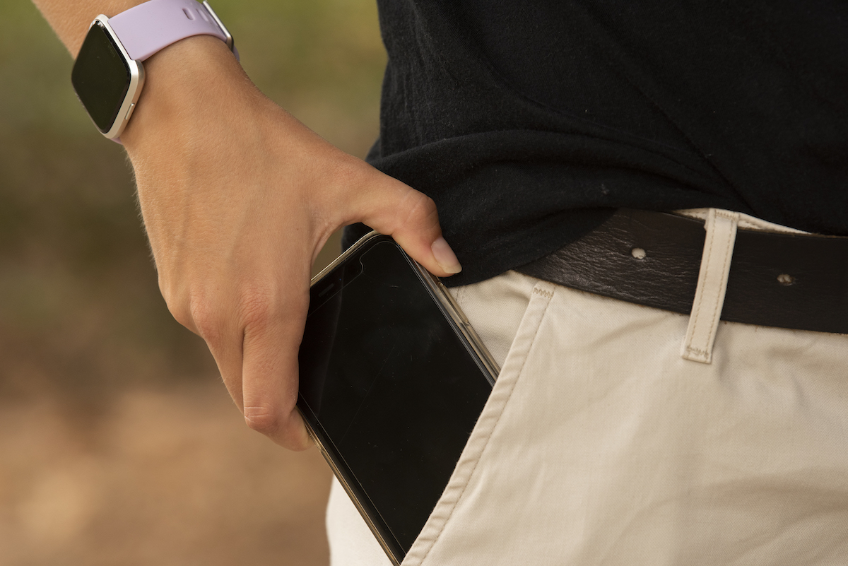 A person wearing a smart watch slips a phone into their pocket. 