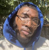 Photo of young black man with glasses and a blue hoodie. 