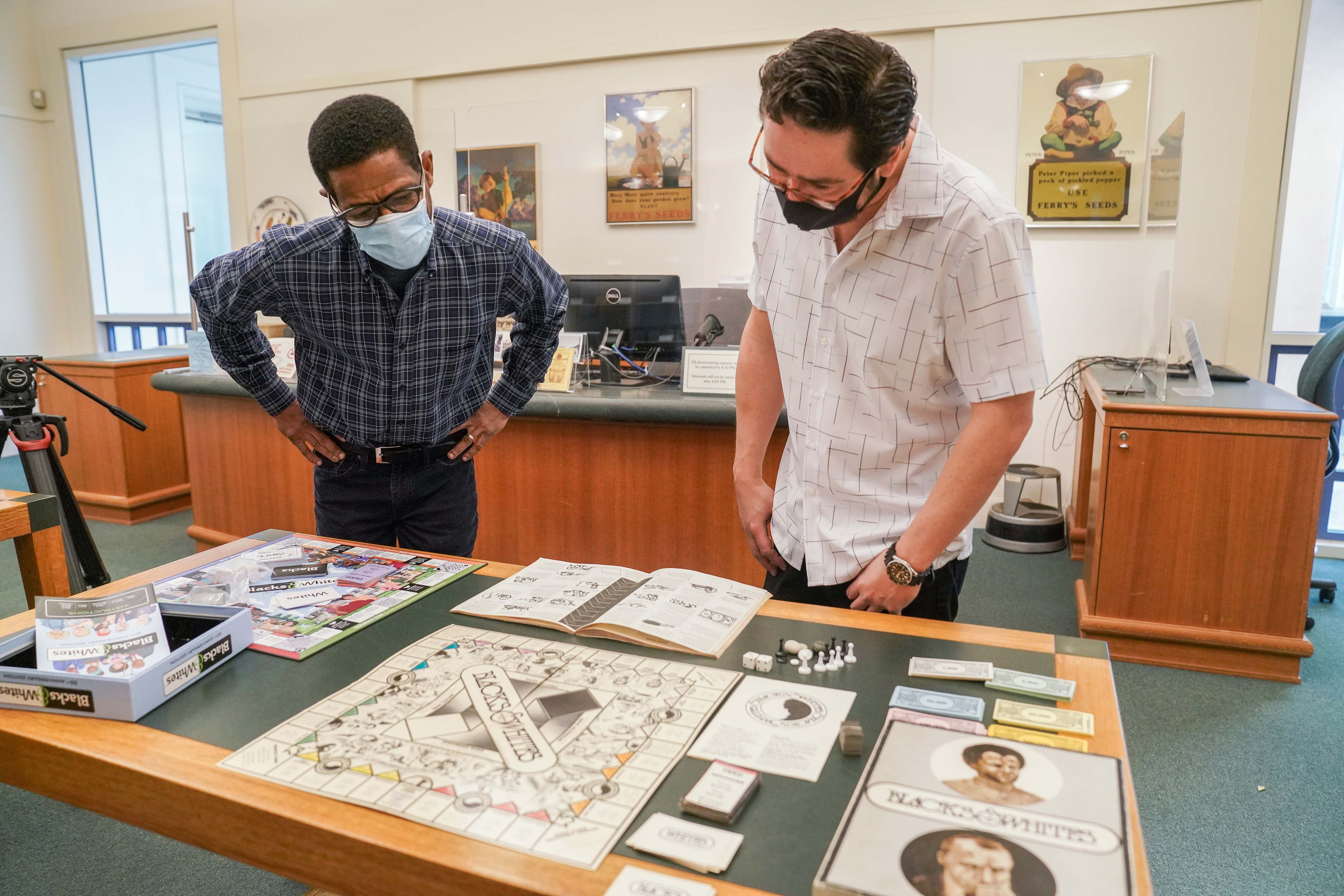Two male professors, wearing face masks, lean over the board games in Special Collections of the UC Davis Library.