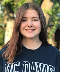 Smiling student with long brown hair and dark blue sweatshirt with UC Davis on front in white