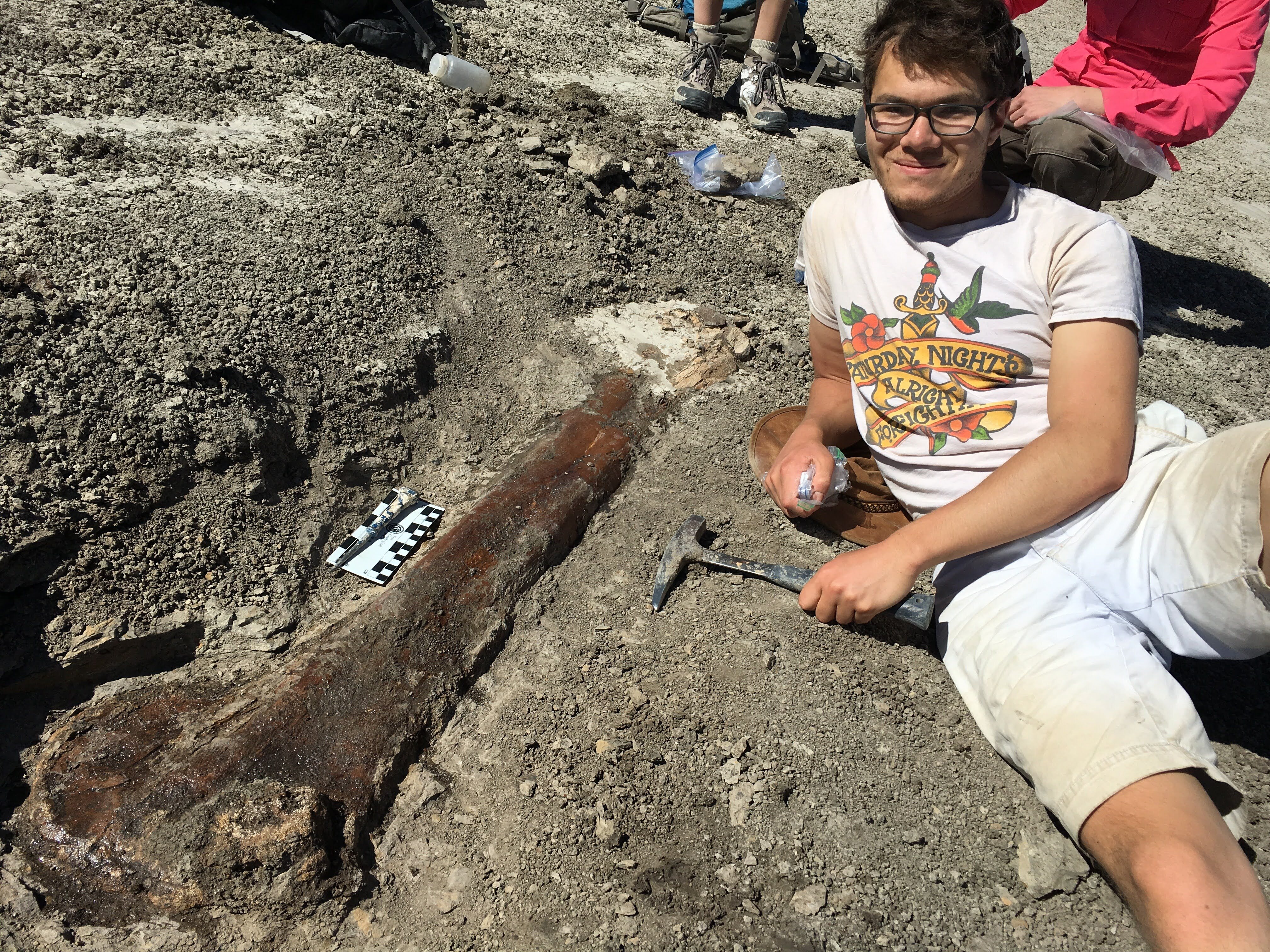 Benjamin Faulkner is lying on the ground next to a large femur bone artifact