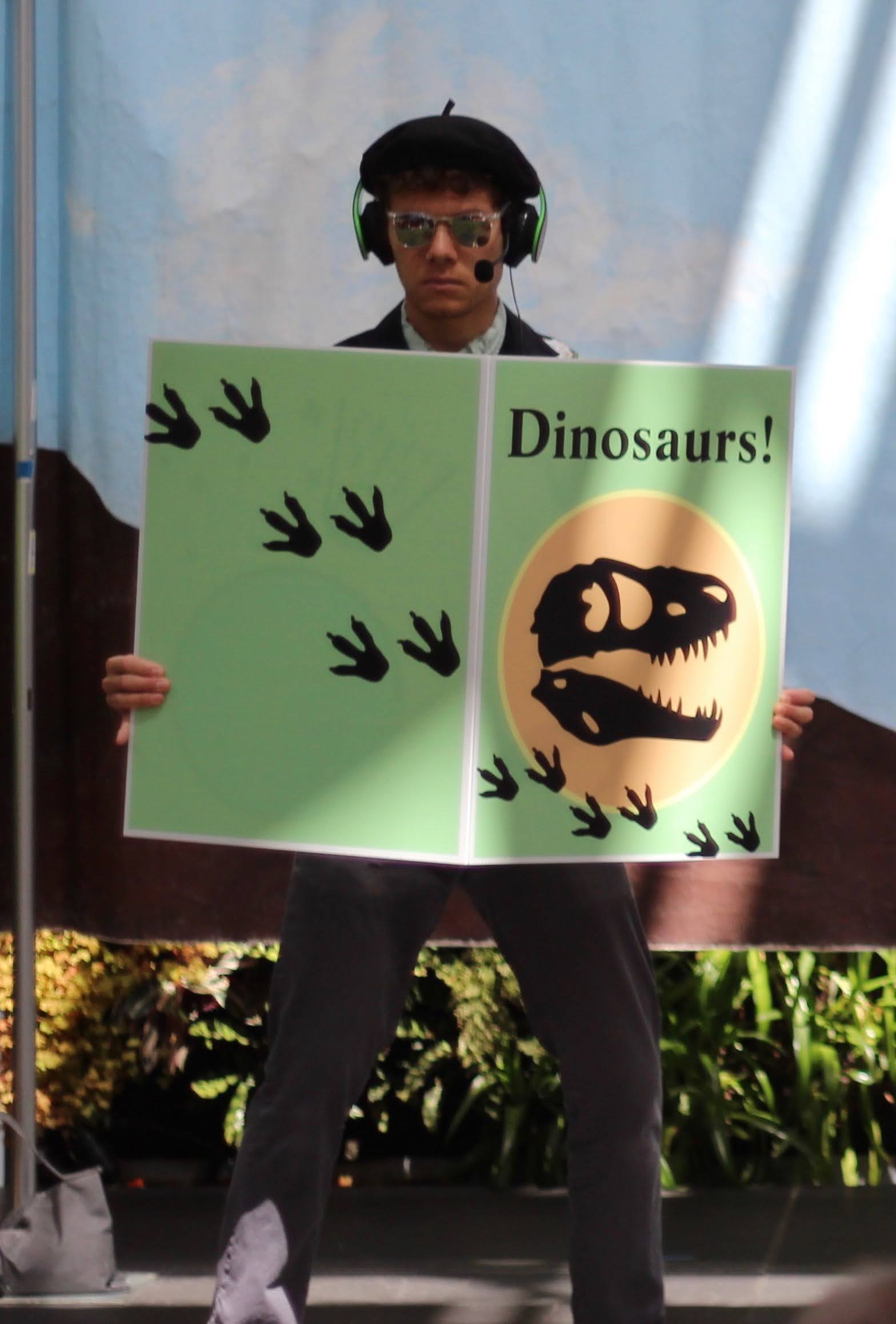 Benjamin Faulkner is standing on a stage with a large green book in his hands that has a picture of a dinosaur on it.