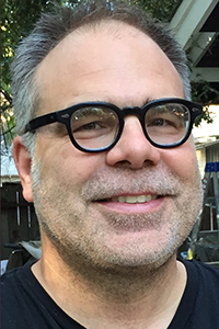 Portrait photo of UC Davis classics lecturer, smiling, wearing glasses, salt and pepper hair and light beard