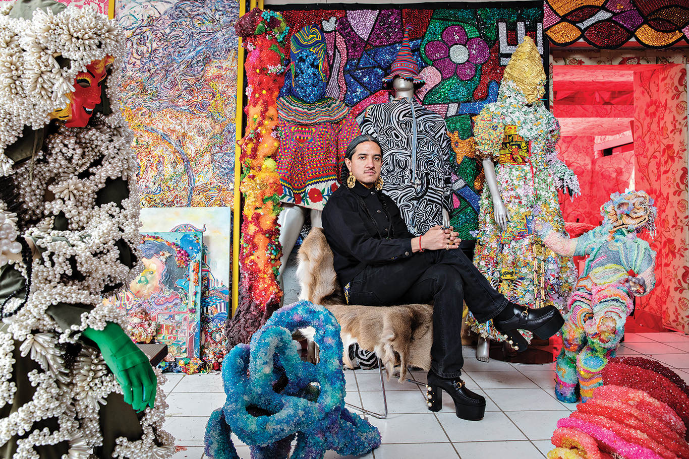 Artist Raúl de Nieves seated, surrounded by his colorful artwork.
