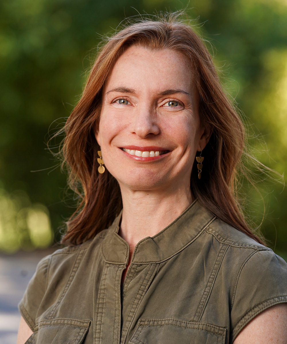 Portrait photo of Amanda Guyer, smiling, green trees in background.