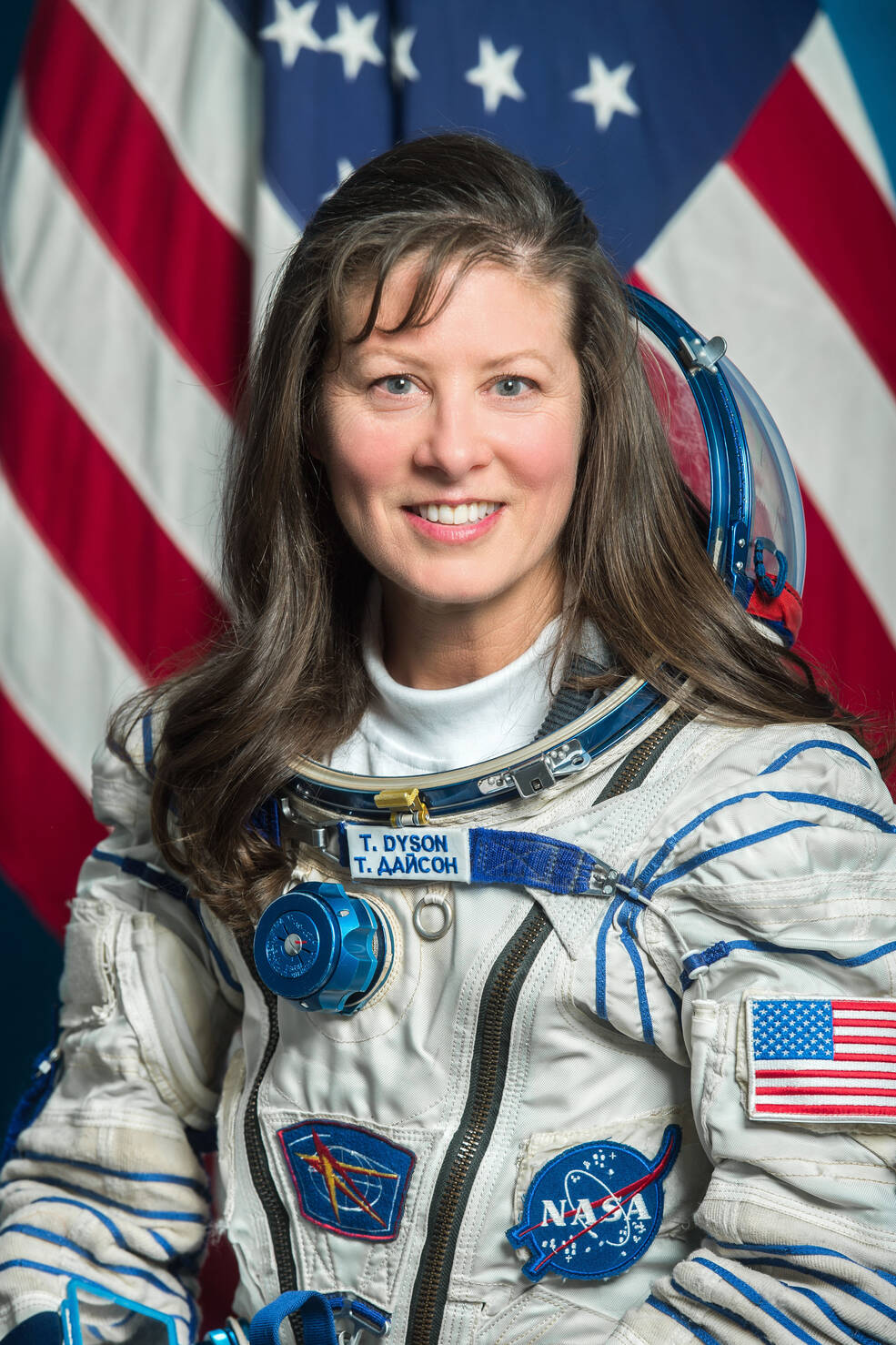 Astronaut Tracy Dyson is wearing her NASA space suit and sitting in front of the American flag 