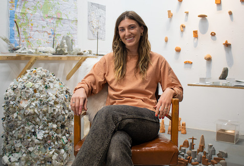 image of woman in brownish shirt, with shoulder length hair seat, with scupltures around her