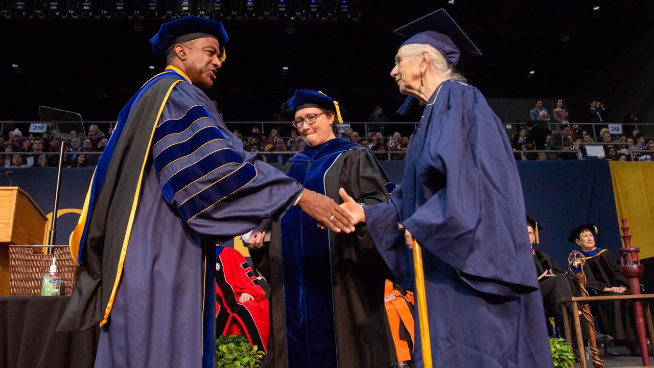 Photo of elderly woman in UC Davis graduation robes shaking hands with chancellor on commencement stage