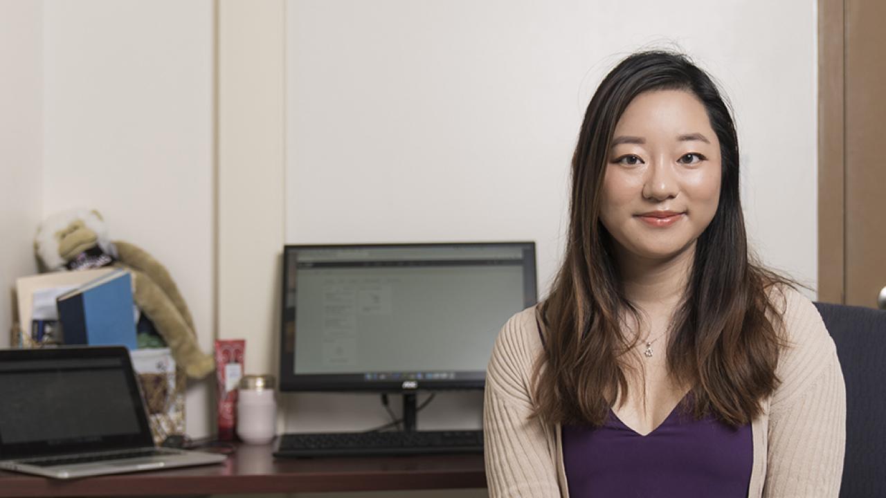 Photo of UC Davis graduate student in front of her desk, computer behind her. 