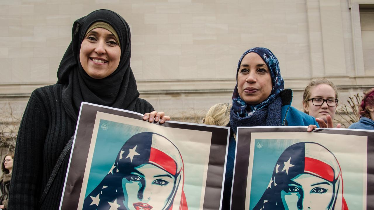 Two Muslim women holding posters of woman wearing stars and stripes hijab