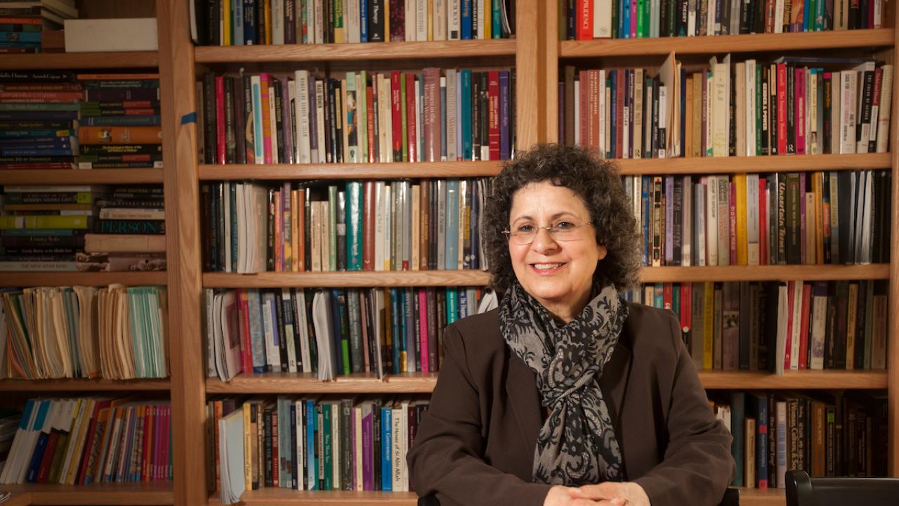 UC Davis professor emeritus, sitting with hands folded, in front of shelves filled with books