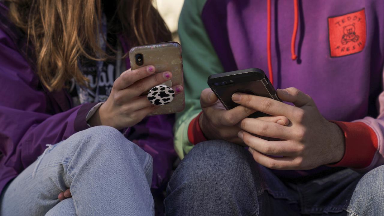 Two students look at their cell phones in a close up photo