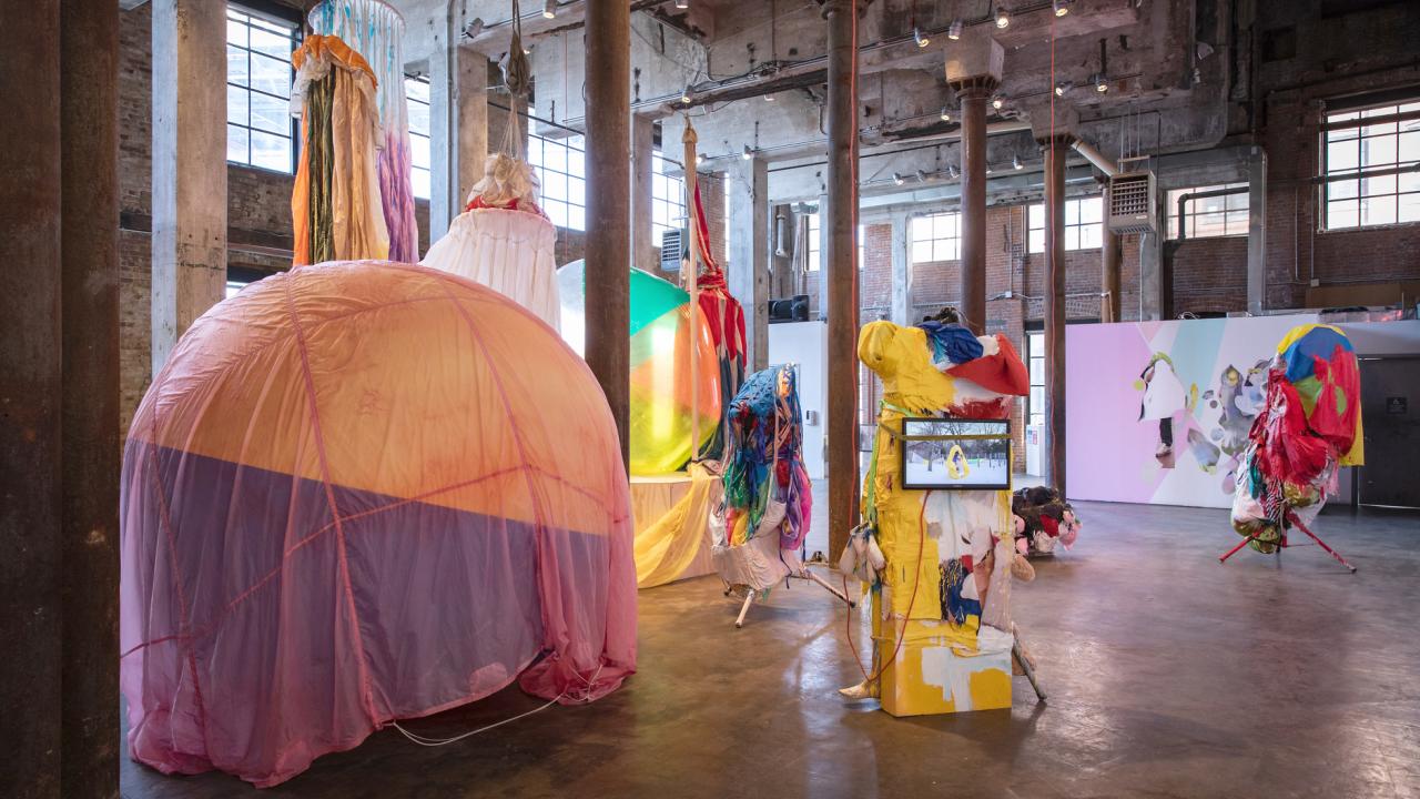 Large pieces of colorful artwork are displayed in a giant warehouse setting 