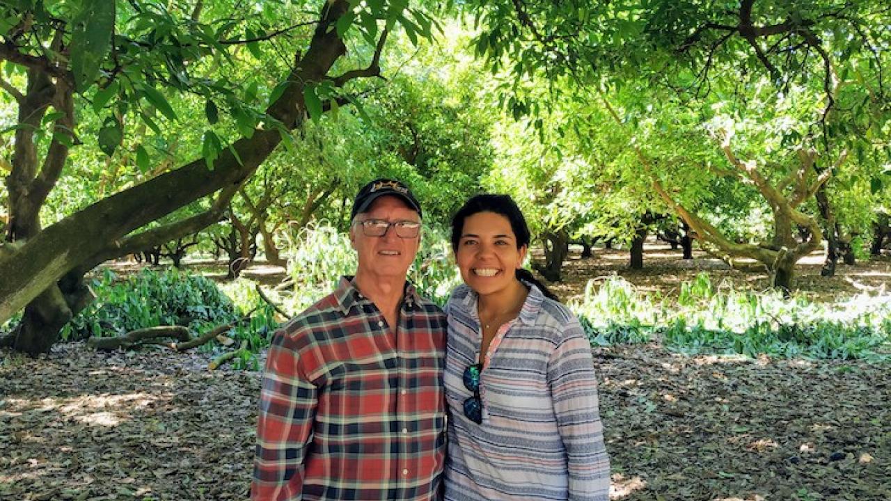a man and woman standing side by side in an orchard