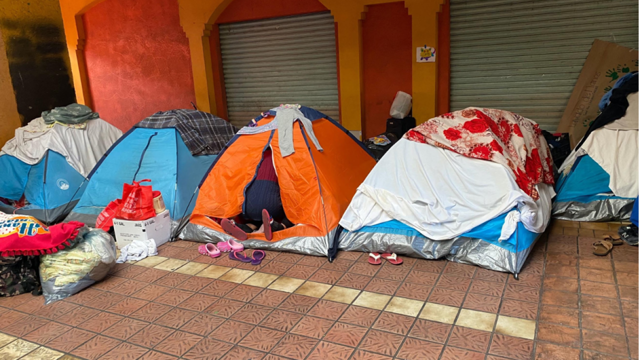 Several tents lined up on a title floor against a stucco wall