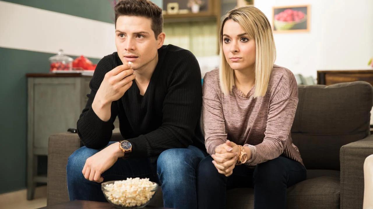 Two people sit and watch television. 
