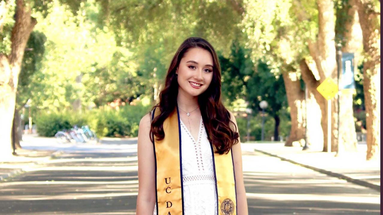 Photo of UC Davis alumna standing near the Quad and wearing her graduationstole