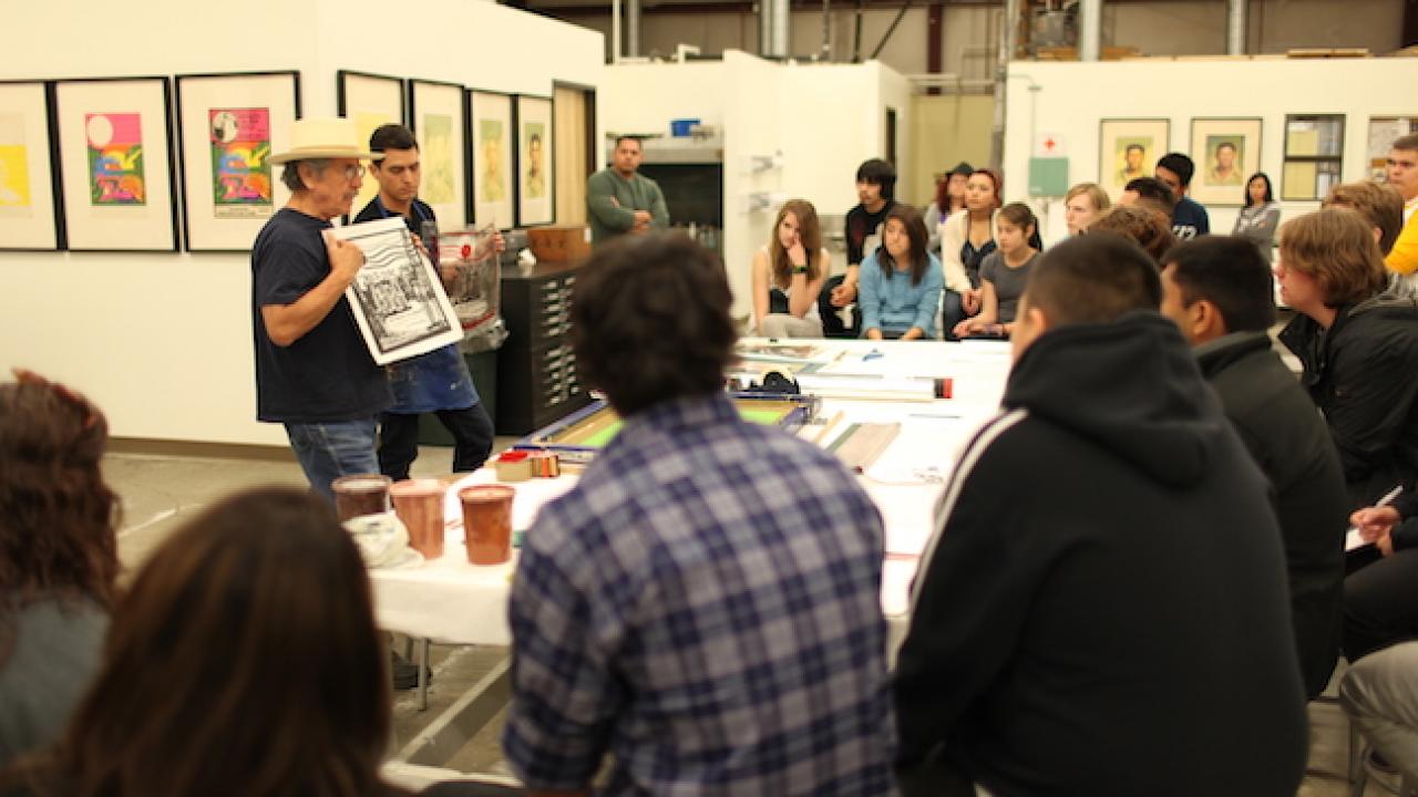 Image of two men (Malaquis Montoya and Carlos Jackson) standing in front of a group of young people showing prints they made
