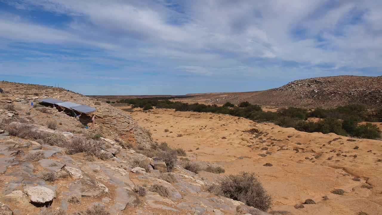 Arid scence in South Africa with shade cloth covering archaeological site on the left.