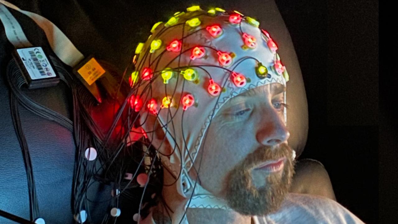 A man wears an EEG cap as he sits down. 