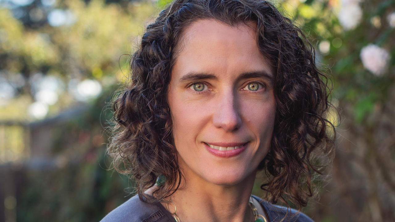 Woman with dark curly hair and green eyes smiles and looks into camera