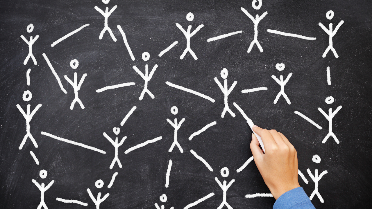 Hand with chalk drawing stick figures and connecting lines on a chalkboard