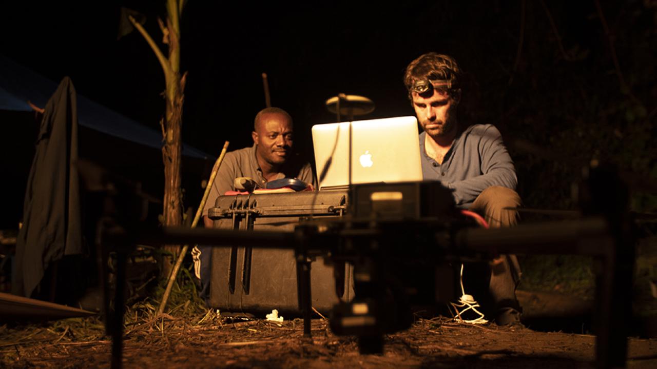 Two gorilla researchers at camp at night looking at a laptop computer