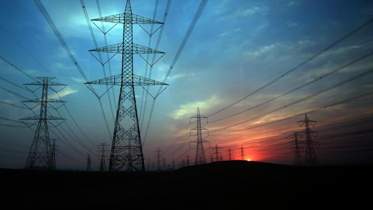 Electric power transmission lines with sun on horizon, glowing pink against a dark blue sky.