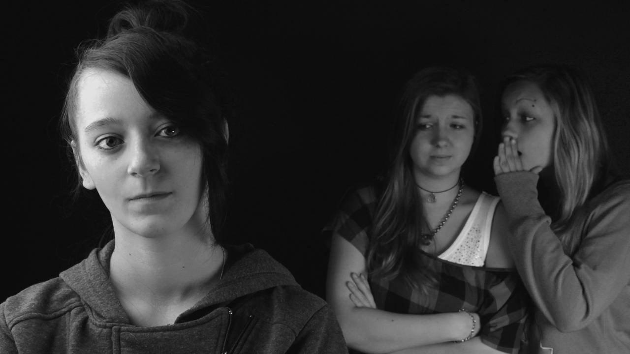 Photo of two girls whispering to each other about a third girl