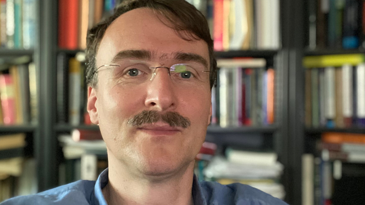 UC Davis economist, wearing glasses and mustache, bookshelves behind nim