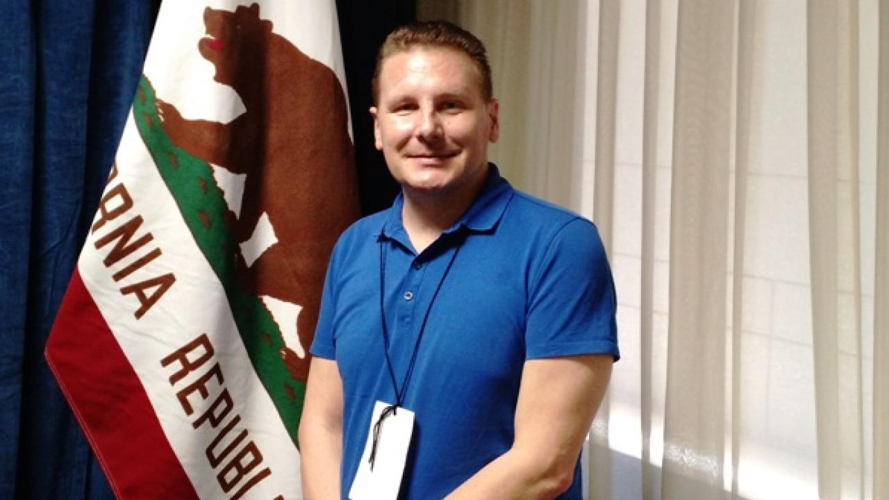 UC Davis College of Letters and Science alumnus Scott Lay, standing in front of the California flag inside a room