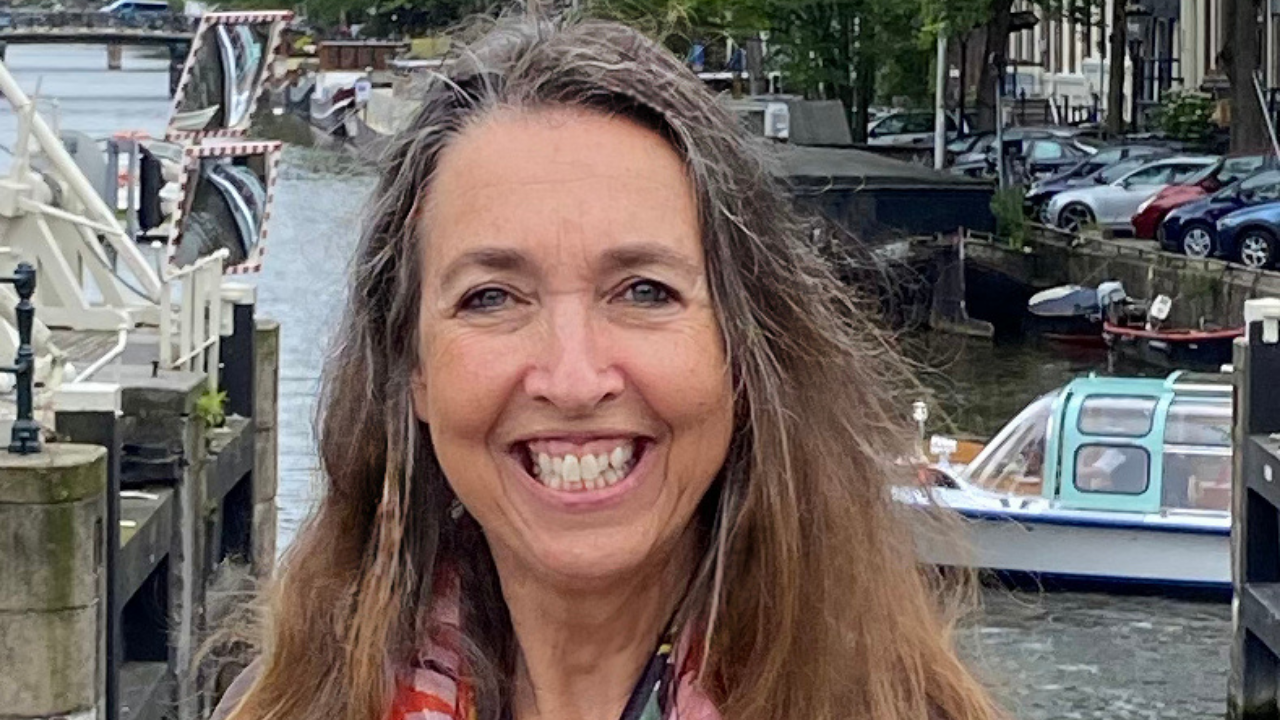 UC Davis psychology professor wearing bright floral scarf and smiling. Behind her is an Amsterdam canal, boats, a dock, bridges and a nearby tree-lined street