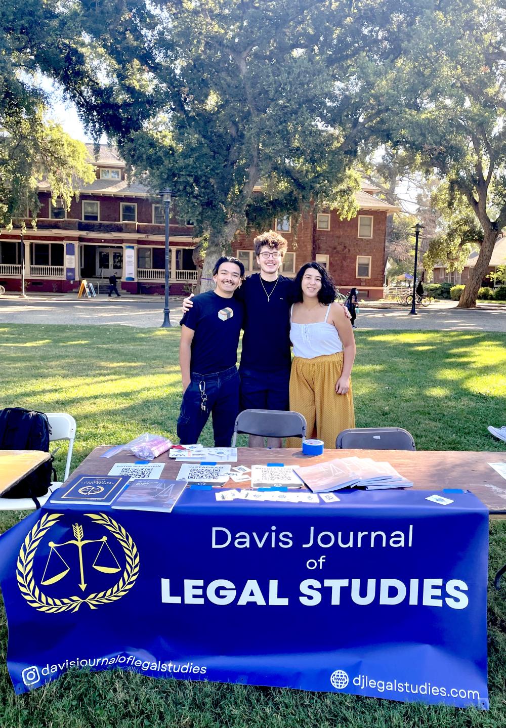 Three students stand side by side in front of a table with a blue sign that reads "Davis Journal of Legal Studies"