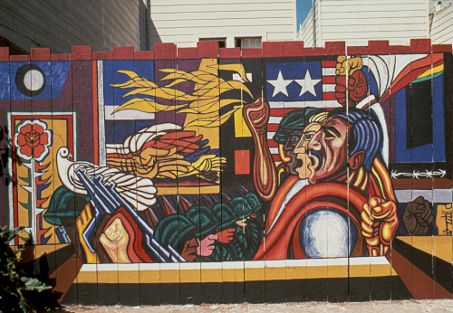 Mural on a fence overlapping faces on the right of men with hands raised in fists in front of  flag of el salvador facing soldiers with guns, dove of peace and abstracted landsacpe
