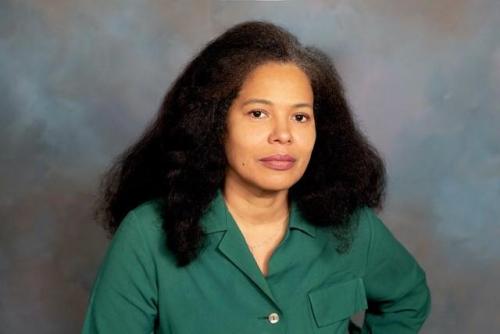 Women with light brown skin, dark shoulder length hair wearing medium green top against  neutral medium gray background 