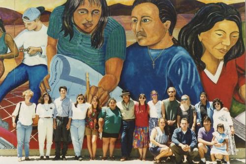 Malaquis Montoya stands in front of a mural with his students beside him