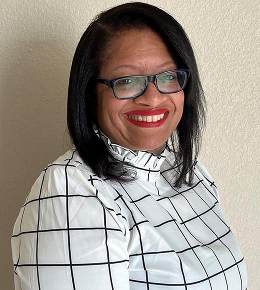 Smiling Black woman with glasses, shoulder-length hair parted on side, and top with high collar in ivory and thin black plaid lines