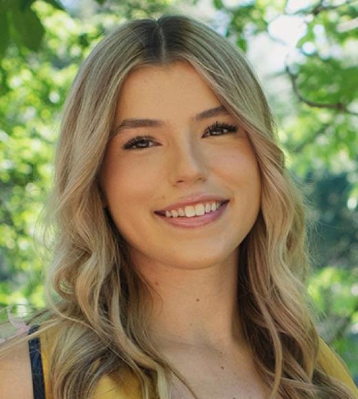 Smiling young woman with long blond hair and green trees in background