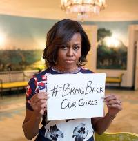 woman with dark hair, brown skin in red and blue floral dress holding up a sign reading "Bring Back our Girls