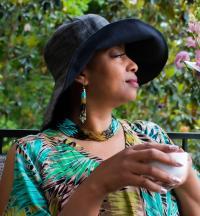 woman facing right, wearing large dark hat, aqua blouse holding cup