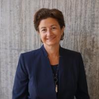 woman with dark hair, dark jacket in front of gray wall