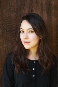 head and shoulder of a woman with dark hair, dark blouse, dark backtround