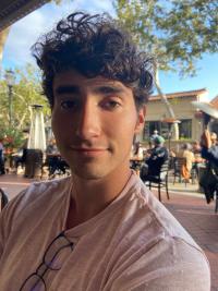 Photo of young man with thick dark hair wearing t shirt outdoors