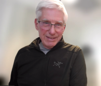 Astronomer Tony Tyson wearing a dark gray jacket in front of a blurred background.