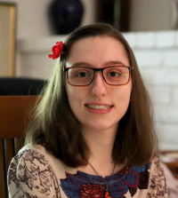 Smiling female student Zoe Eiselt with shoulder-length brown hair pulled off to side of forehead with red flower pin, wearing eye glasses