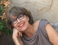 woman wearing gray loose blouse with chin length brown/gray hair , dark framed glasses, with head titled smiling 